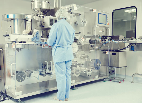 A person in protective clothing monitors a piece of equipment in a biopharmaceutical setting